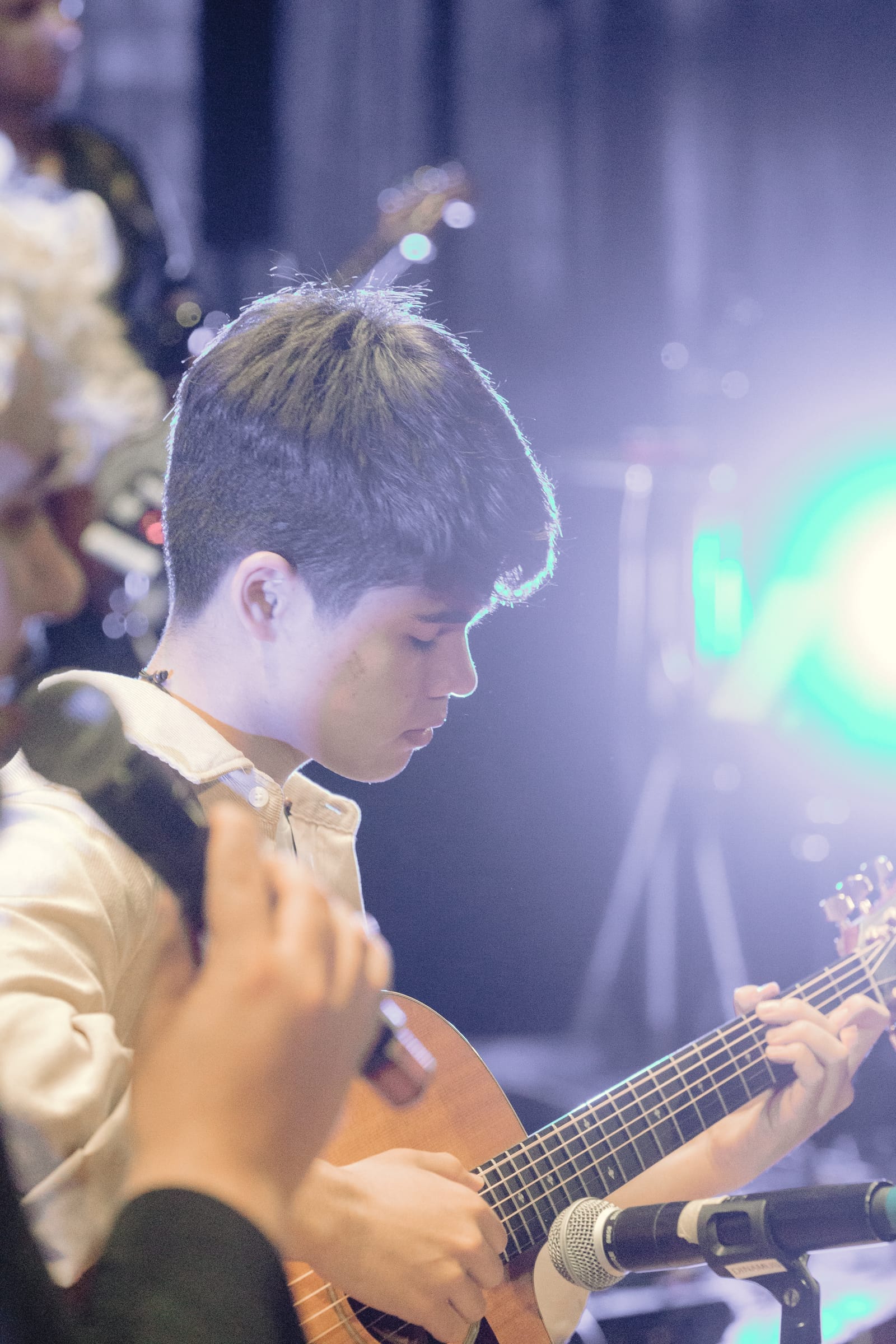 Aluno da Dias Music tocando violão no palco, sob luz de show